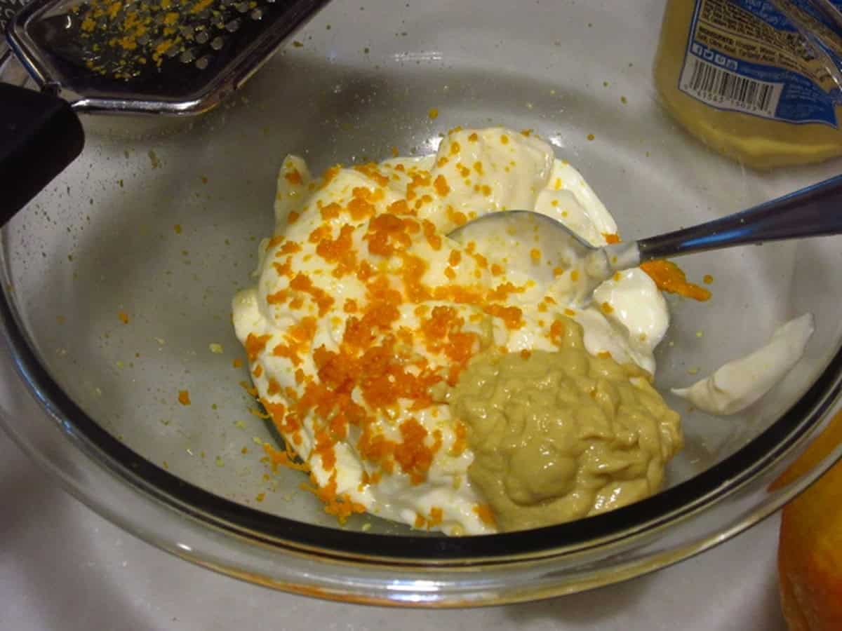 Orange zest and mustard in a glass bowl with mayonnaise.