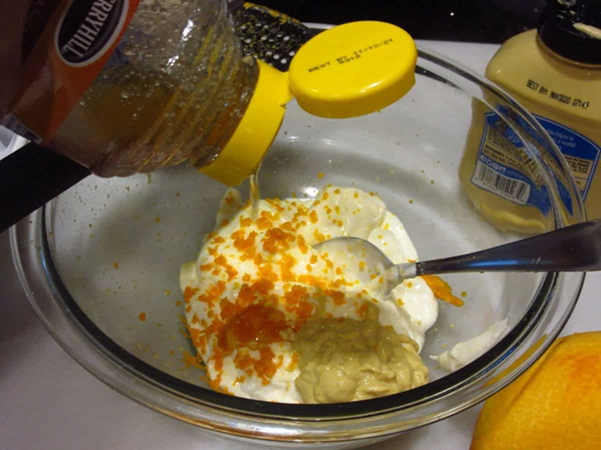 Honey being squeezed into a bowl with mayo and orange zest.
