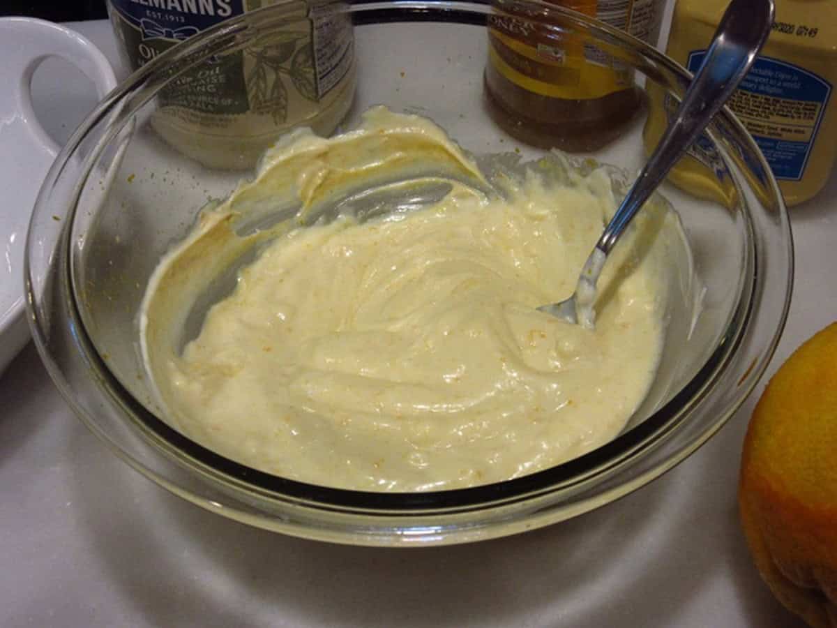 A mayonnaise-based orange dipping sauce in a glass bowl with a spoon.