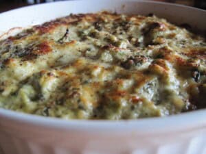 A white casserole dish filled with Cheesy Spinach Artichoke Dip topped with melted cheese.