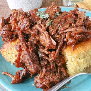 Tasty cooking pulled beer braised beef brisket over some squares of cornbread on a blue plate.
