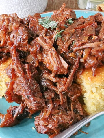 Tasty cooking pulled beer braised beef brisket over some squares of cornbread on a blue plate.