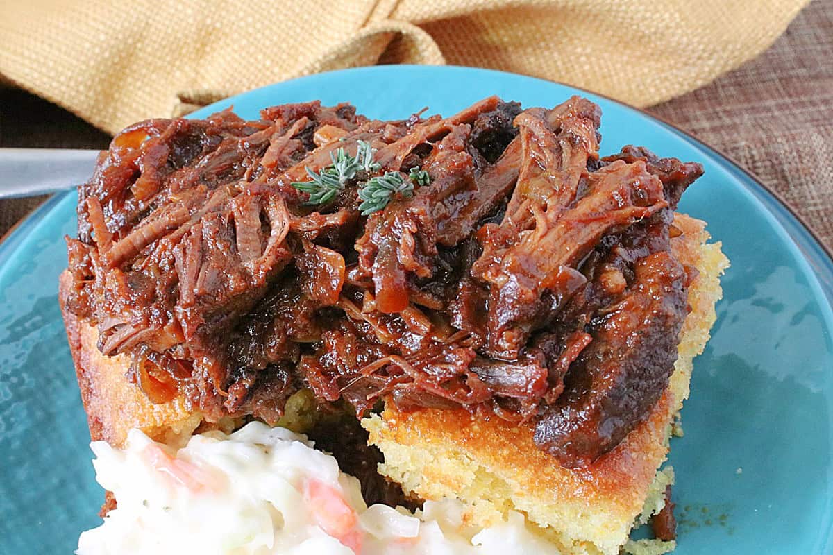 A delicious meal of beer braised beef brisket on a plate with coleslaw on the side along with cornbread.