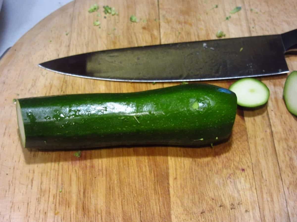 A green zucchini on a cutting board with a knife.