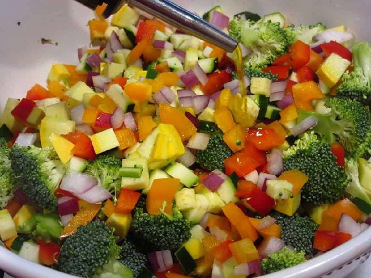 A bunch of colorful, diced veggies in a bowl with olive oil being poured over them.