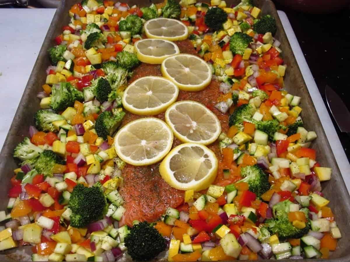 Colorful diced vegetables surrounding an uncooked trout fillet on a sheet pan.