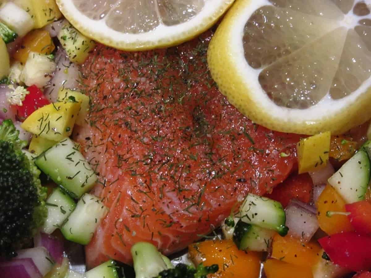 An uncooked piece of rainbow trout topped with dill and lemon slices.