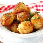 A white bowl filled with crispy, golden arancini balls topped with chopped basil.