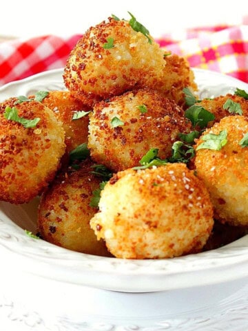 A white bowl filled with crispy, golden arancini balls topped with chopped basil.
