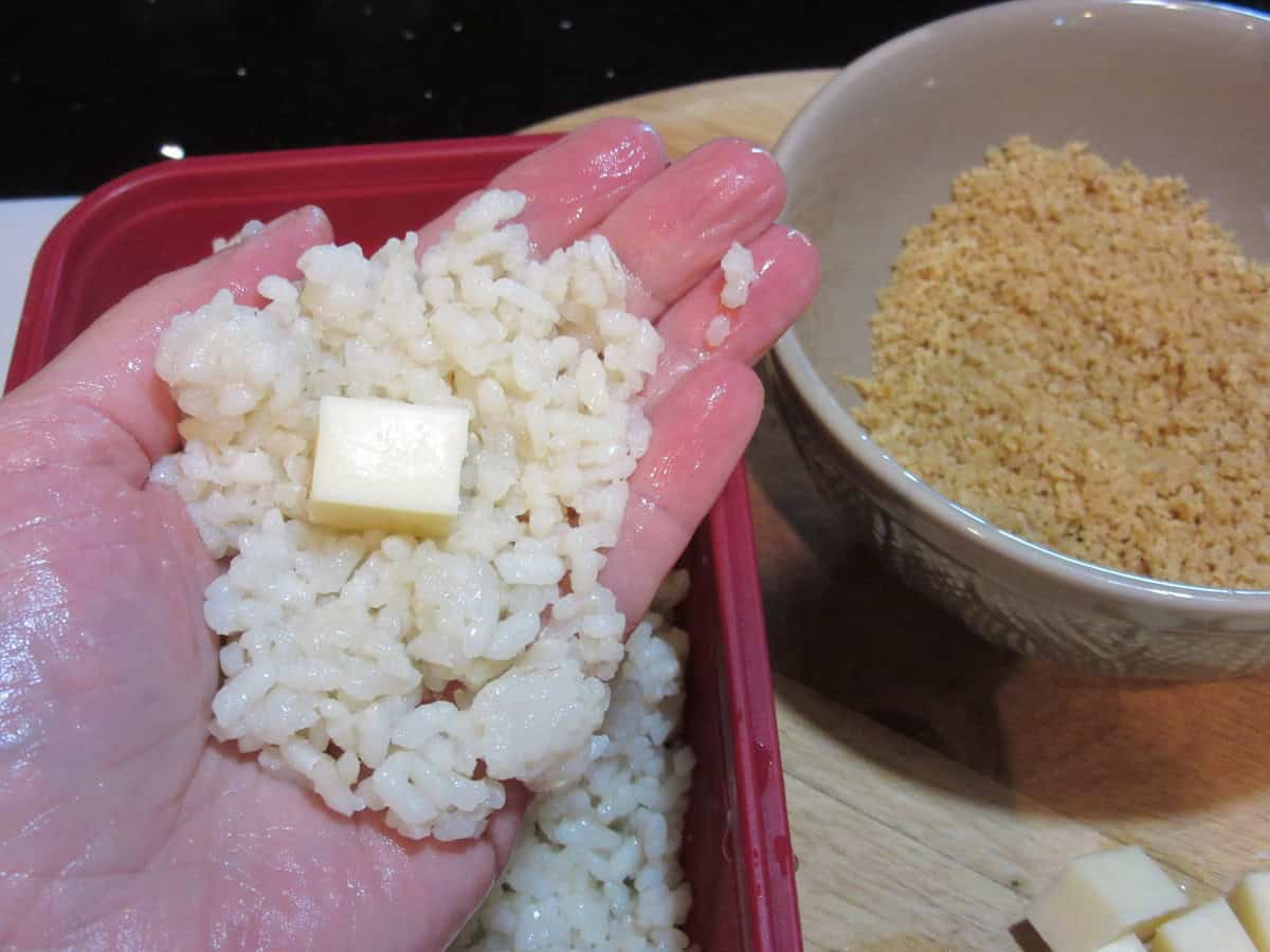 A square of mozzarella cheese in the middle of some flattened rice on a hand to make arancini balls.