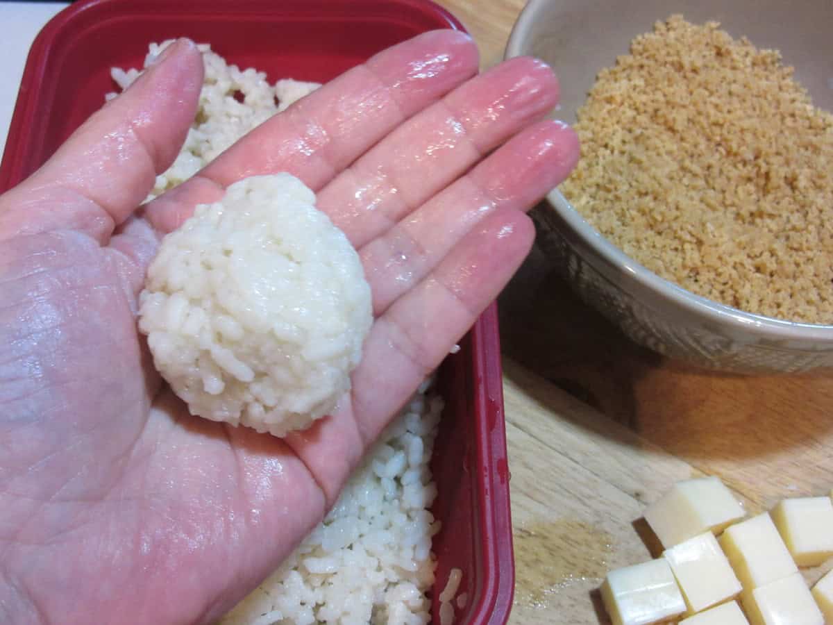 A wet hand holding a cheese encased arancini ball.