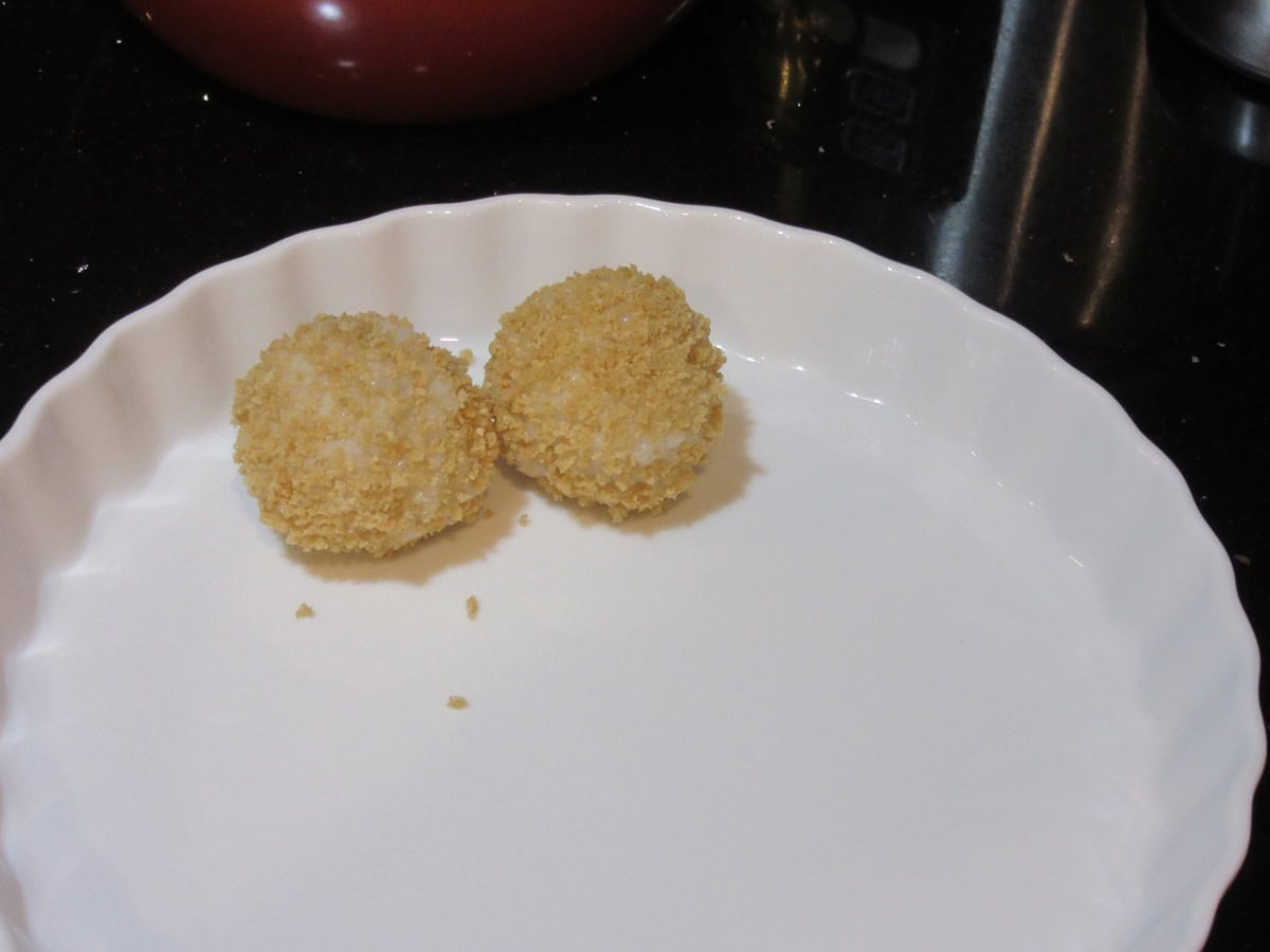 Two panko crumb covered arancini balls before frying in a white dish.