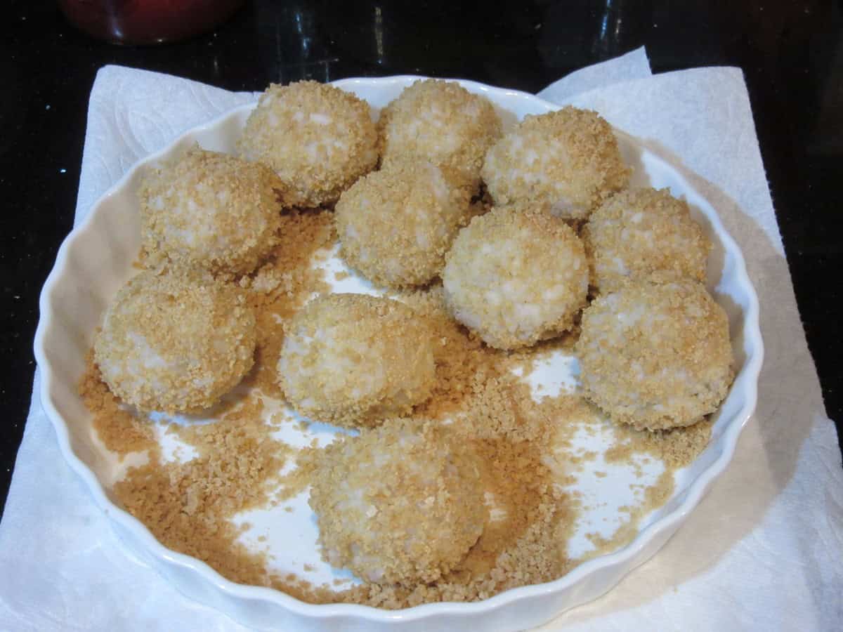 A shallow white dish filled with panko covered arancini balls before being fried.