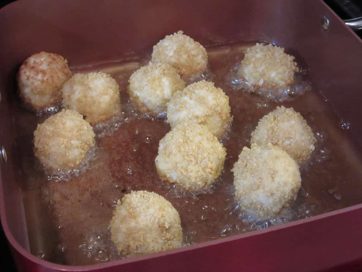A bunch of panko covered arancini balls frying in a skillet.