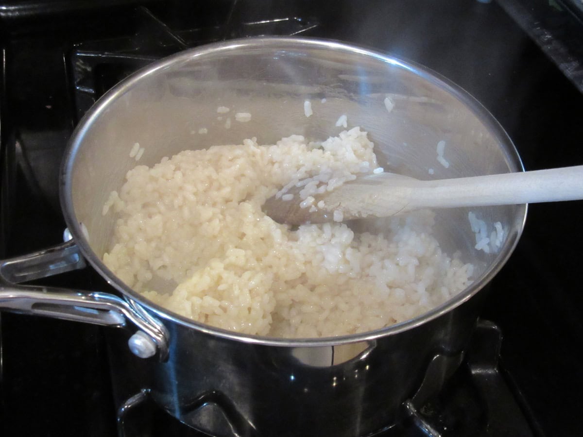 Cooked arborio rice in a saucepan along with a wooden spoon.