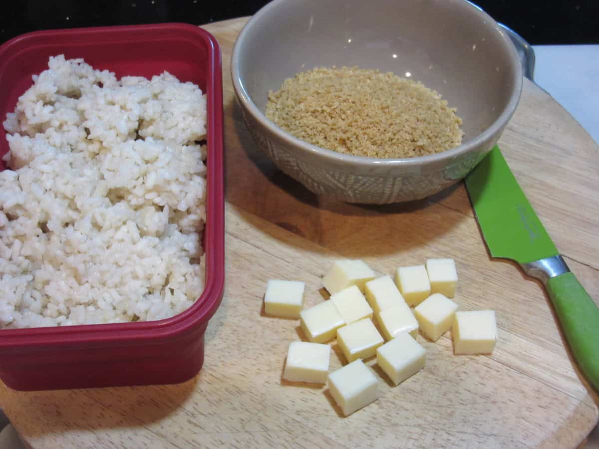 A dish of cooled rice, bowl of panko crumbs and cubes of mozzarella cheese.