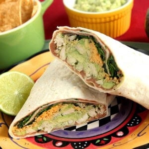 A chicken and avocado wrap that's been cut in half on a colorful Mexican-inspired plate.