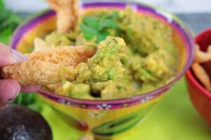 A hand holding a pork rind that's been dipped in homemade guacamole.