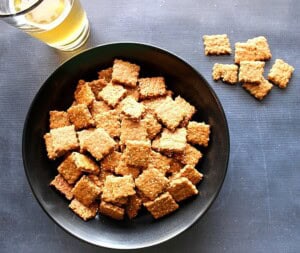 A black bowl filled with homemade sesame seed crackers on a black table.