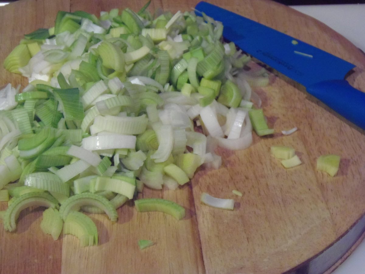 A pile of sliced leeks on a wooden cutting board with a knife.