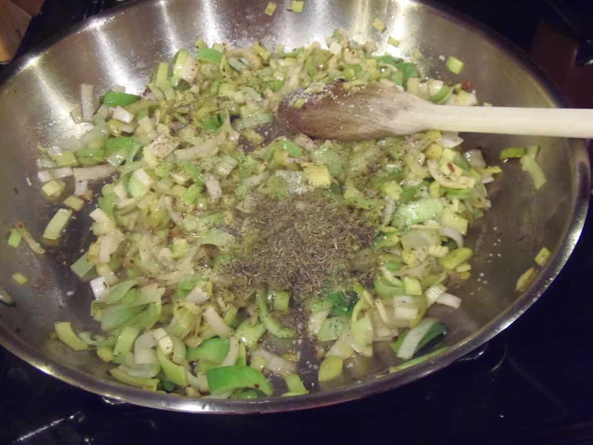 Sliced leeks cooking in a skillet with dried herbs.