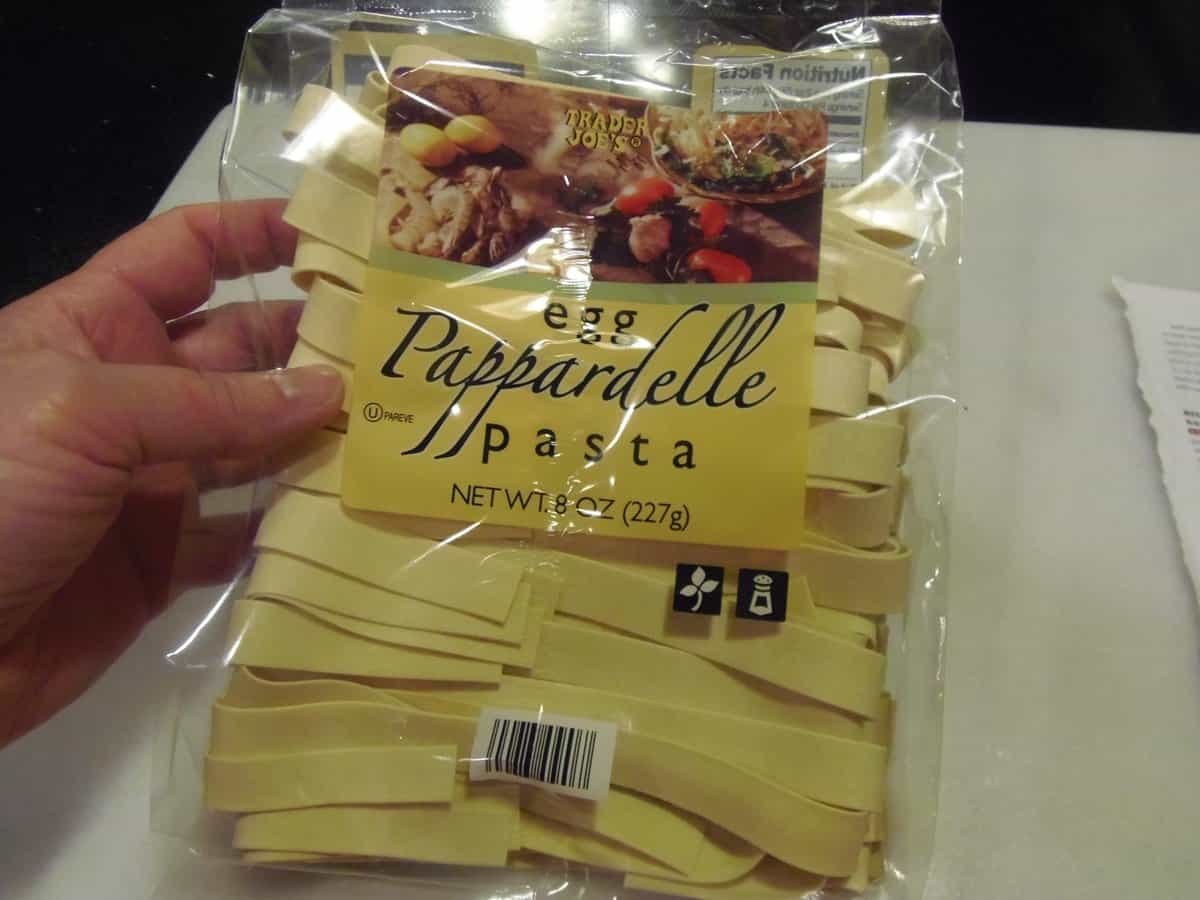 A hand holding a bag of Trader Joes pappardelle pasta.