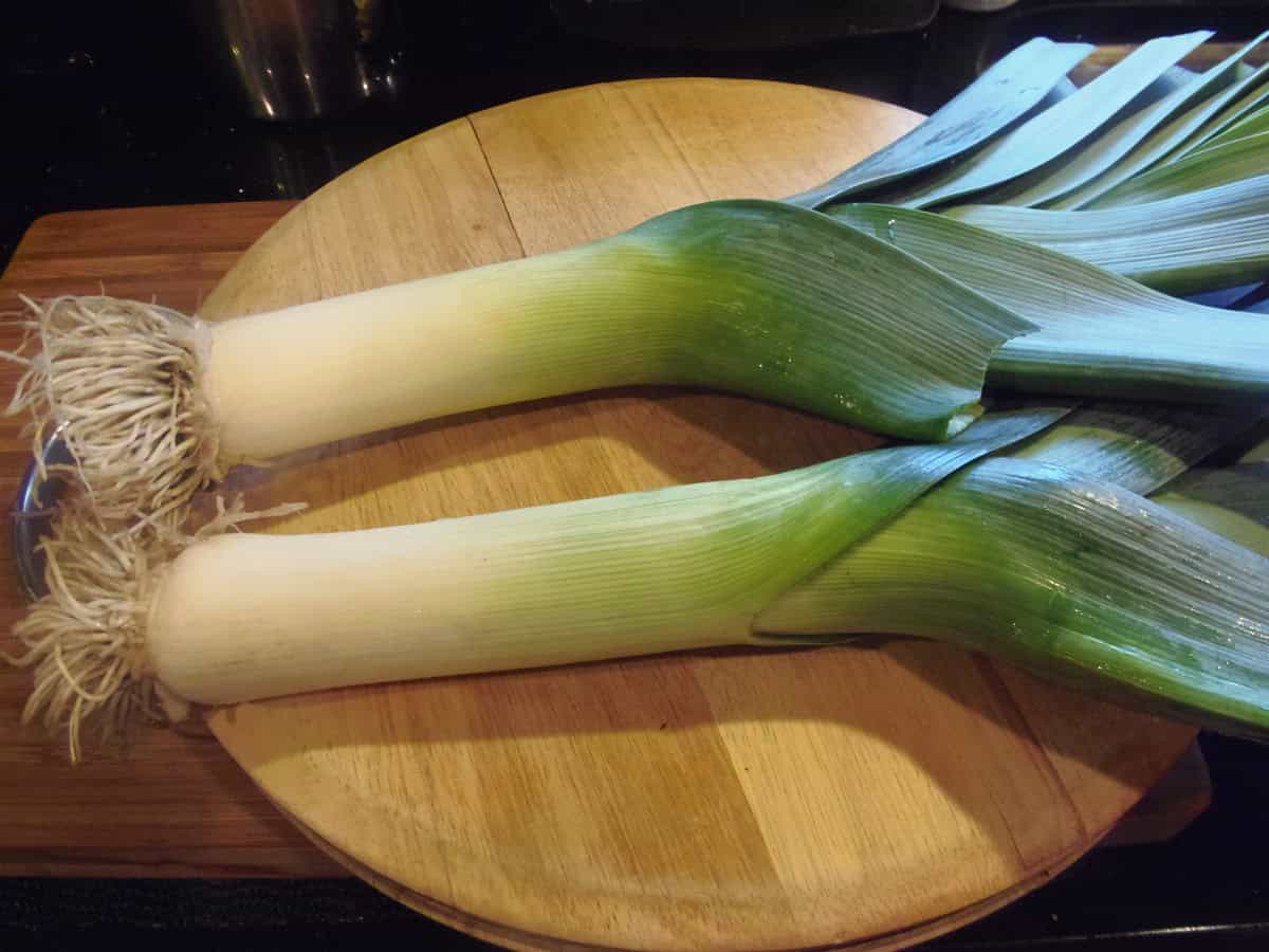 Two large leeks on a round wooden cutting board.