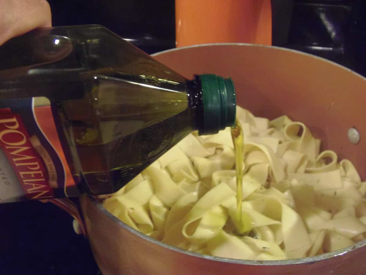 Olive oil being poured into a pot with cooked pappardelle pasta.
