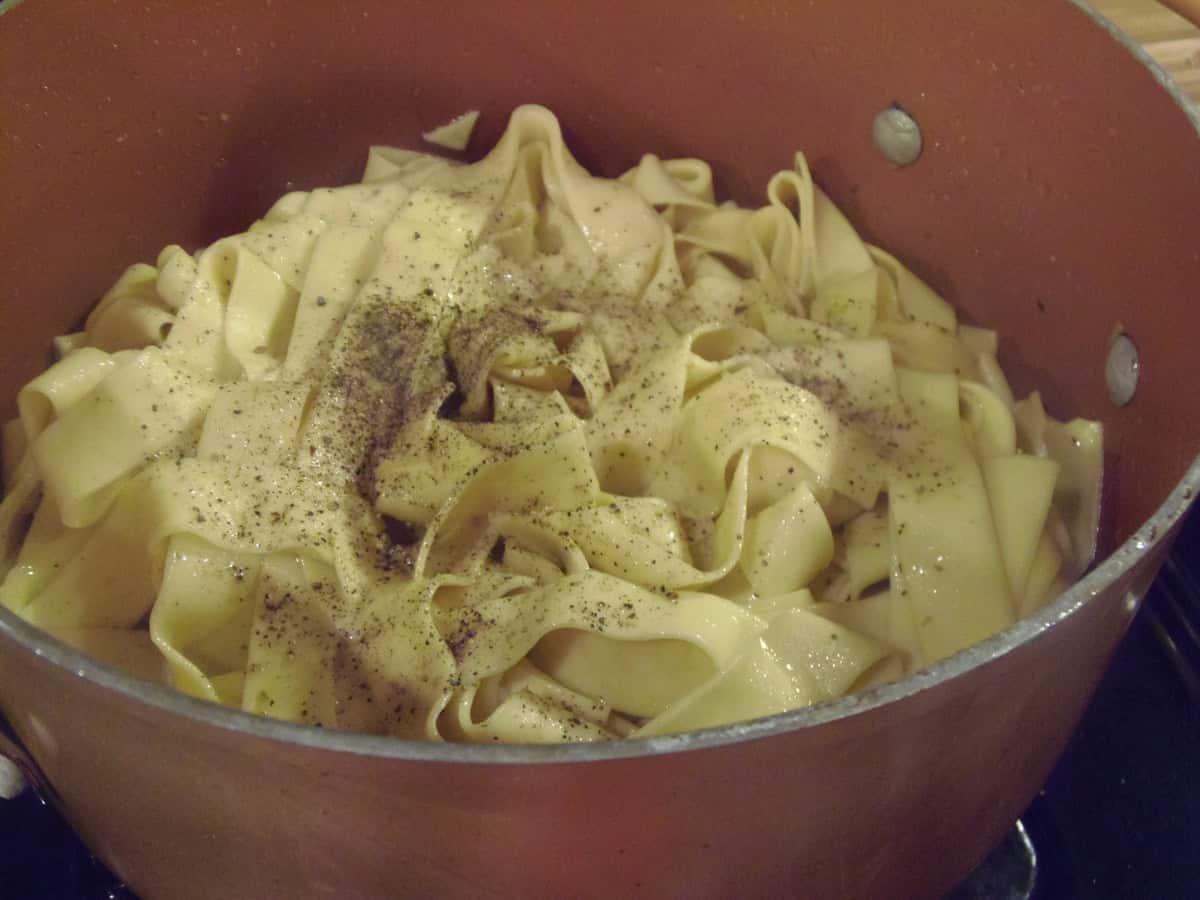 Cooked and drained pappardelle pasta in a pot with salt and pepper.