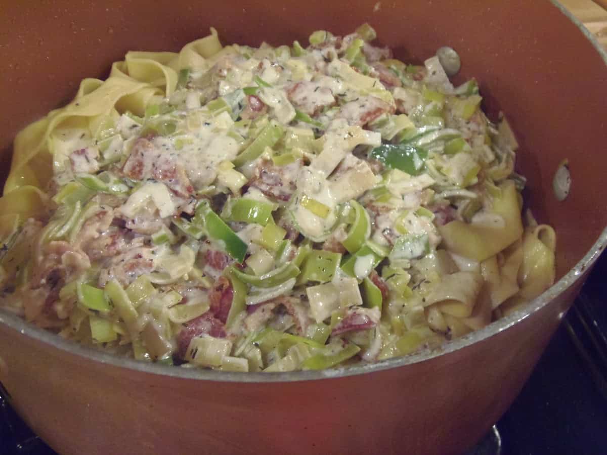 A large pot with cooked pappardelle pasta, leeks, bacon and cream sauce.