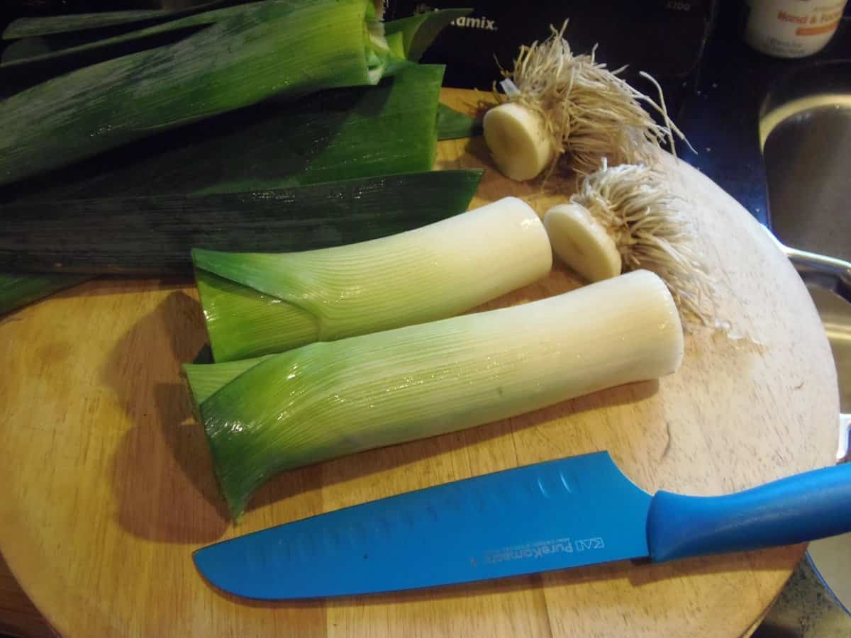 Two leeks on a cutting wooden board with a blue knife.
