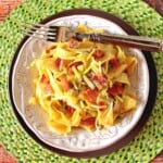 A round green placemat topped with two plates holding one serving of delicious looking pappardelle pasta with bacon and leeks.
