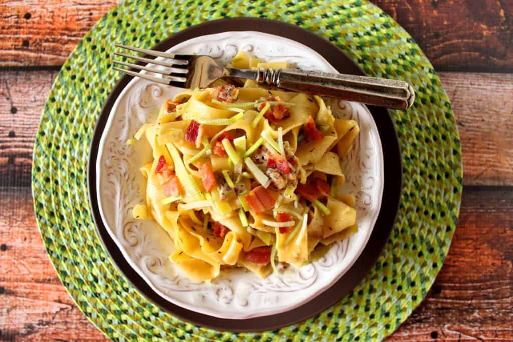 A fork on the side of a plate with a serving of pappardelle pasta.