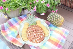 A pineapple-shaped cheeseball on an oval platter with a colorful napkin.