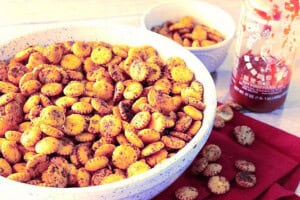 A white bowl filled with sriracha firecracker oyster crackers and a bottle of sriracha on the side.