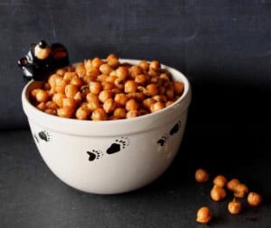 A cute bowl with a bear and bear paws filled with sriracha roasted chickpeas on a black background.