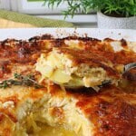 A spoon holding a serving of potatoes au gratin with onions over the casserole dish.