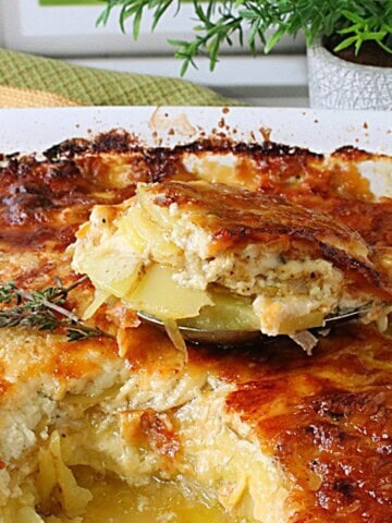 A spoon holding a serving of potatoes au gratin with onions over the casserole dish.