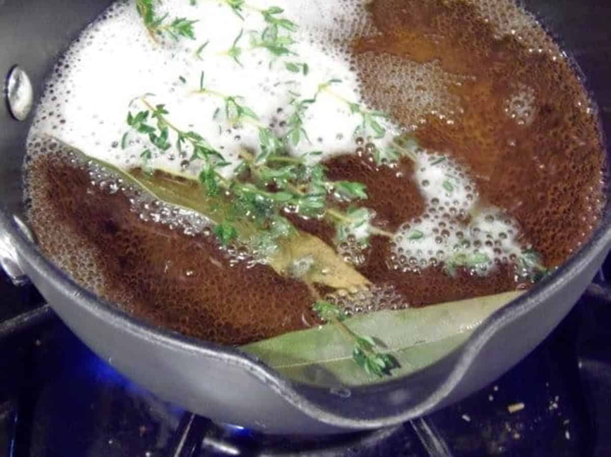 A saucepan on the stovetop with fresh thyme and bay leaves inside.