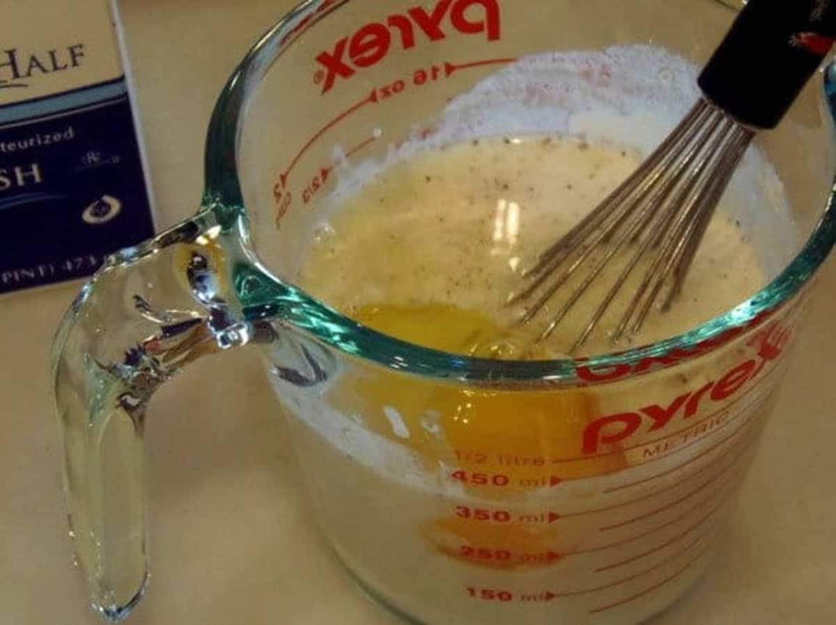 A glass measuring cup with an egg and heavy cream inside.