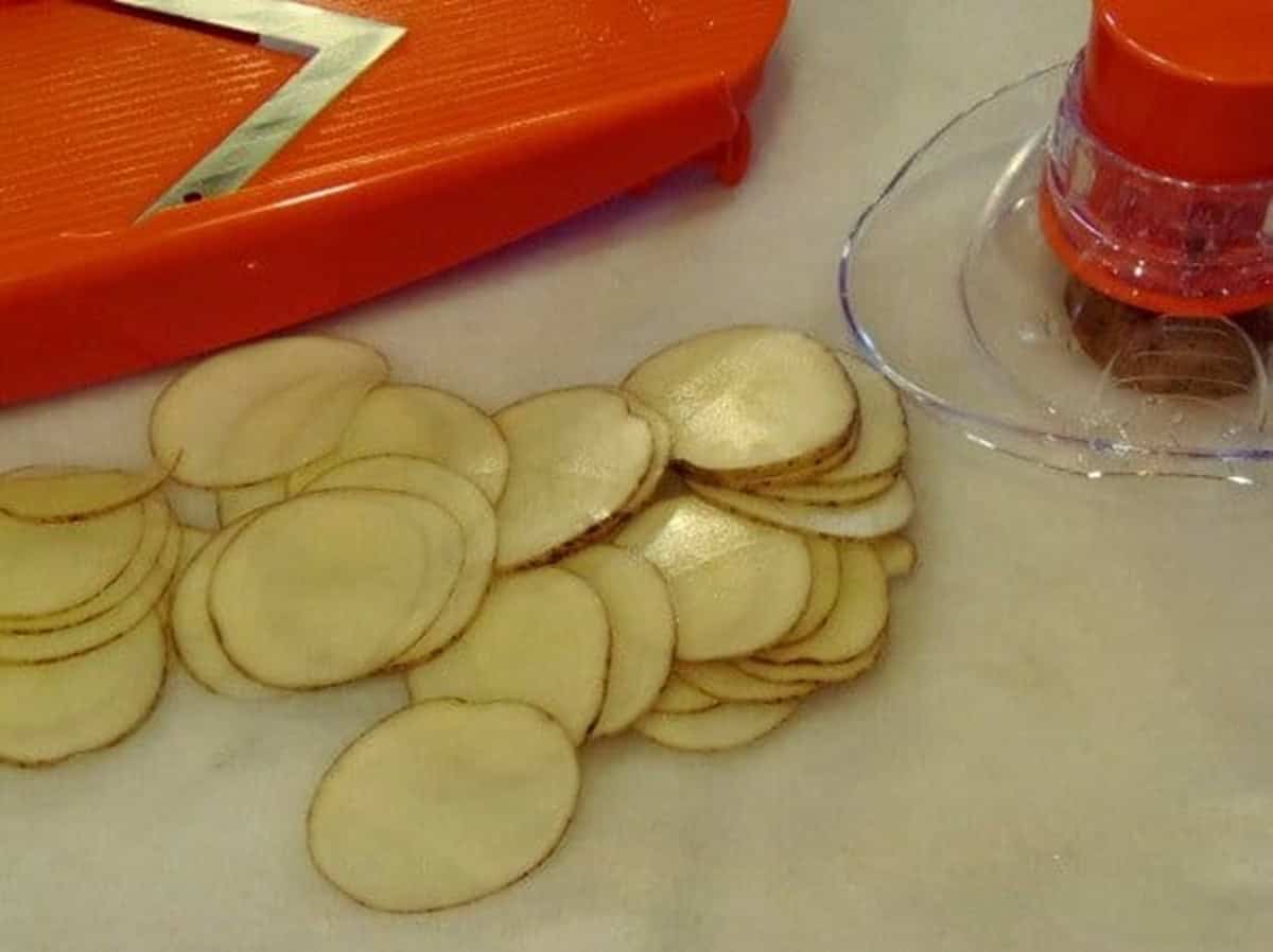 Thinly sliced potatoes on a board with a mandolin next to the potatoes.
