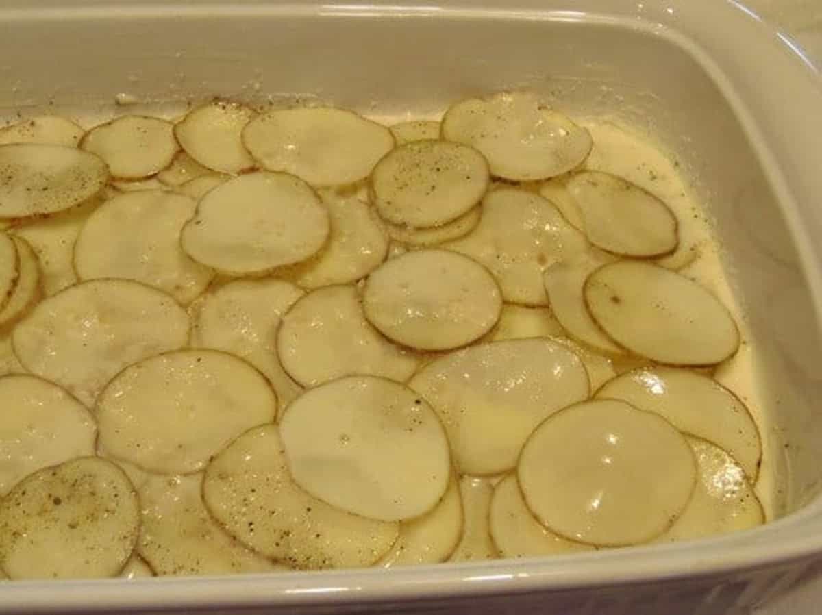A bunch of thinly sliced potatoes in a white rectangle casserole dish.