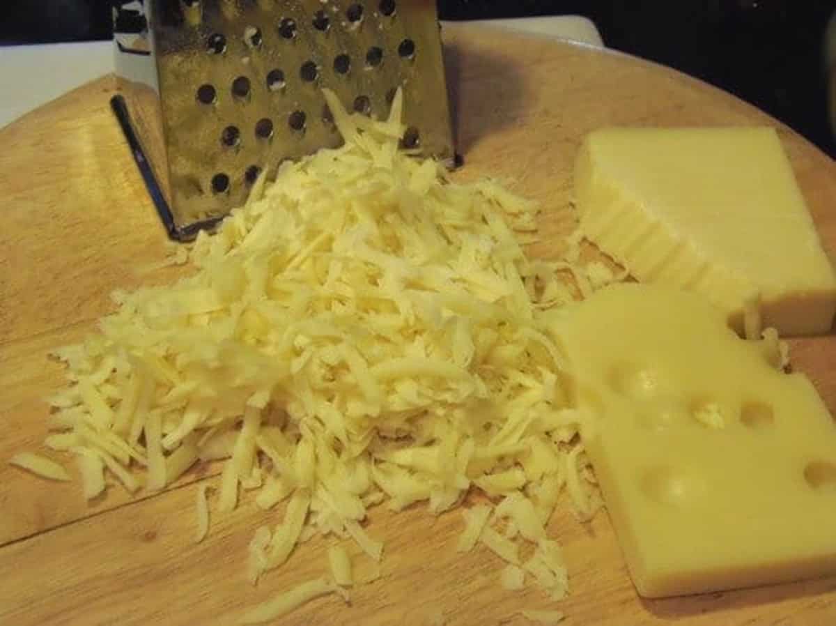 Shredded cheese on a wooden cutting board with a box grater.