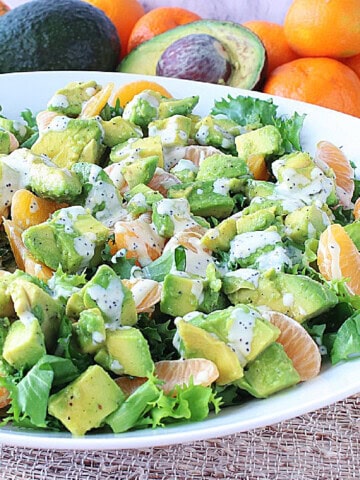 A green and orange avocado and orange salad topped with a poppy seed dressing.