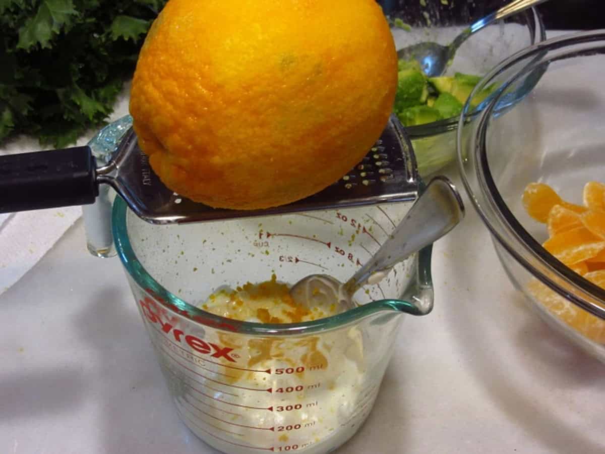 Orange zest being added to a glass bowl using a microplane.