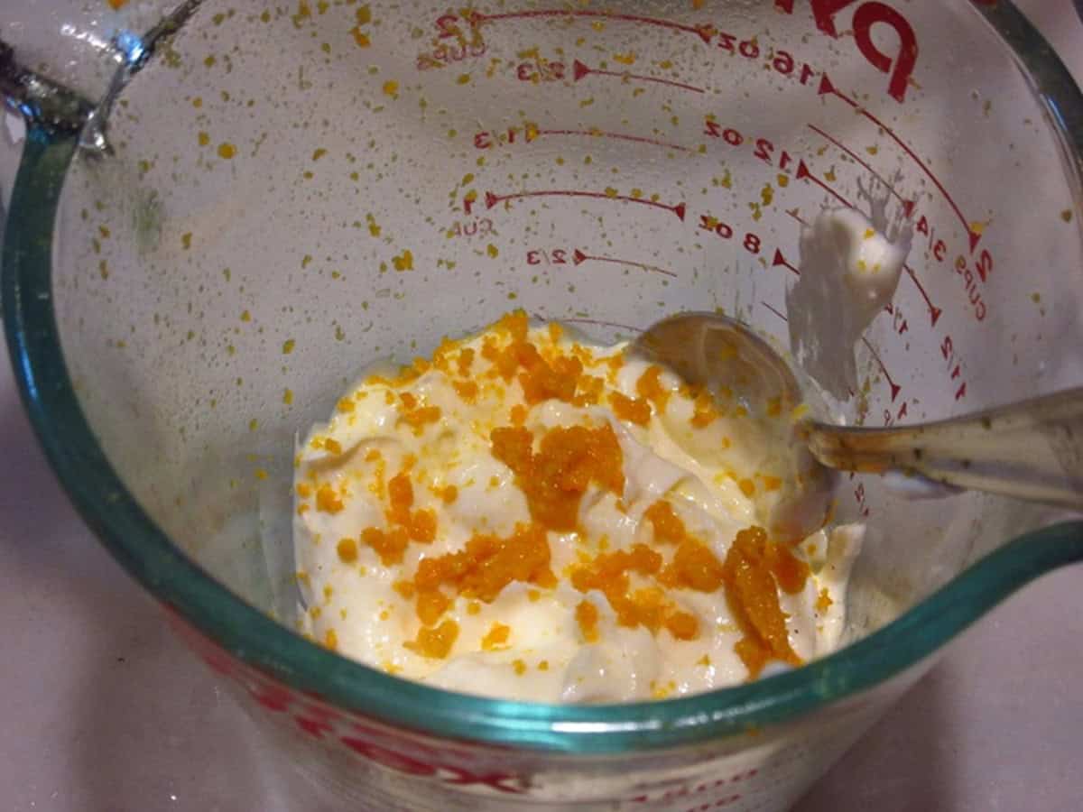 Orange zest and mayonnaise in a glass bowl with a spoon.