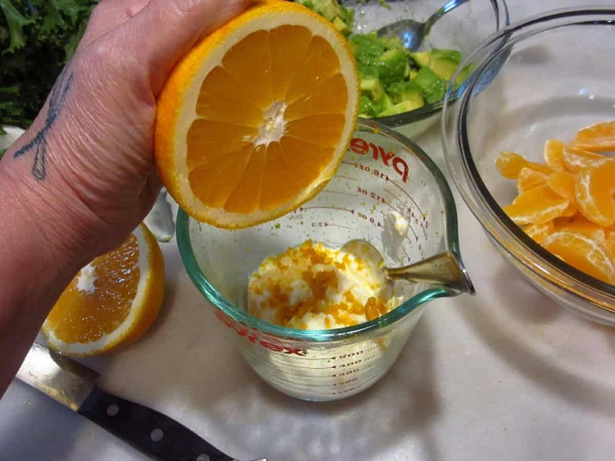 A hand squeezing fresh orange juice in a glass measuring cup.
