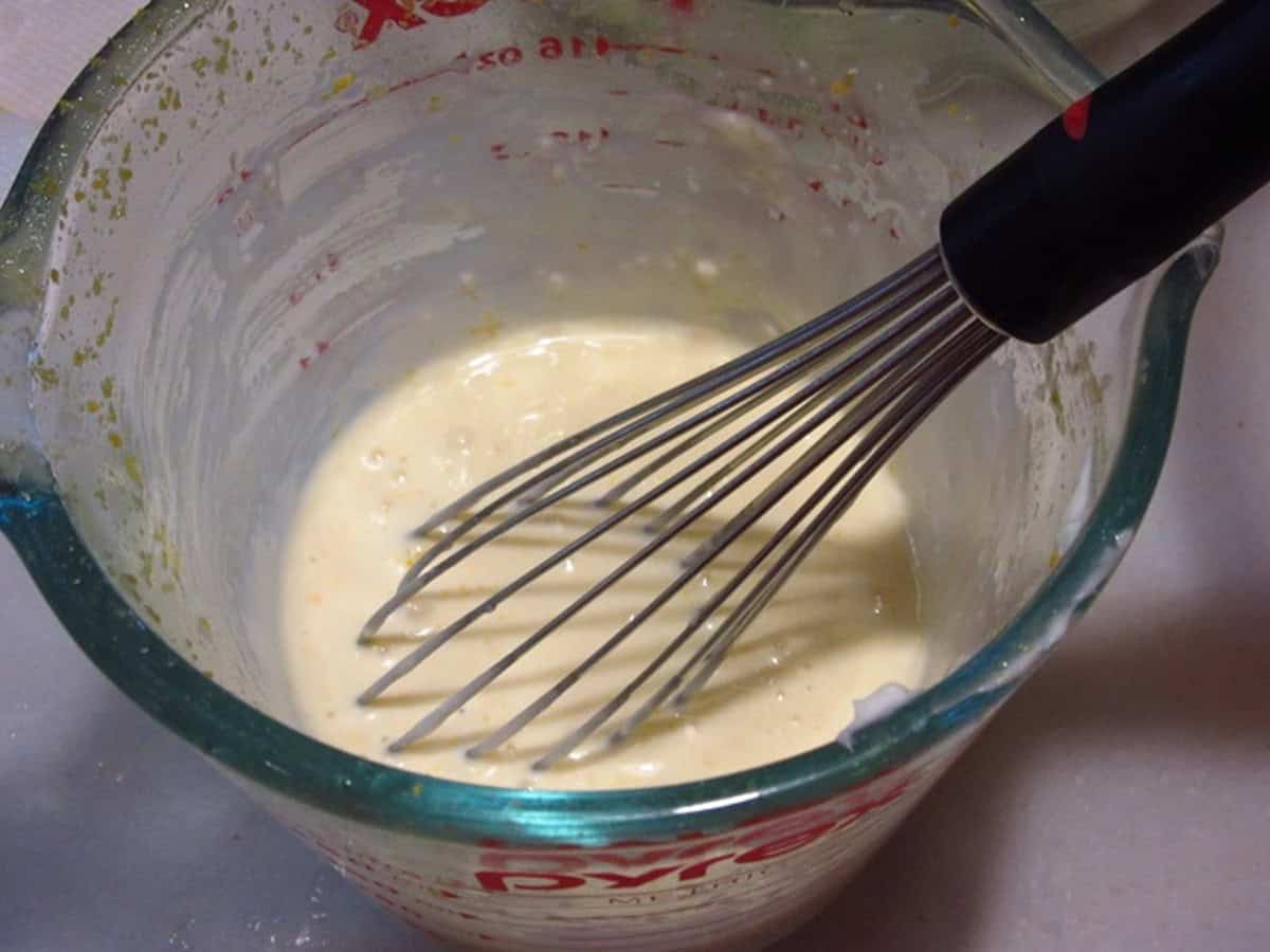 A whisk in a glass measuring cup making salad dressing.