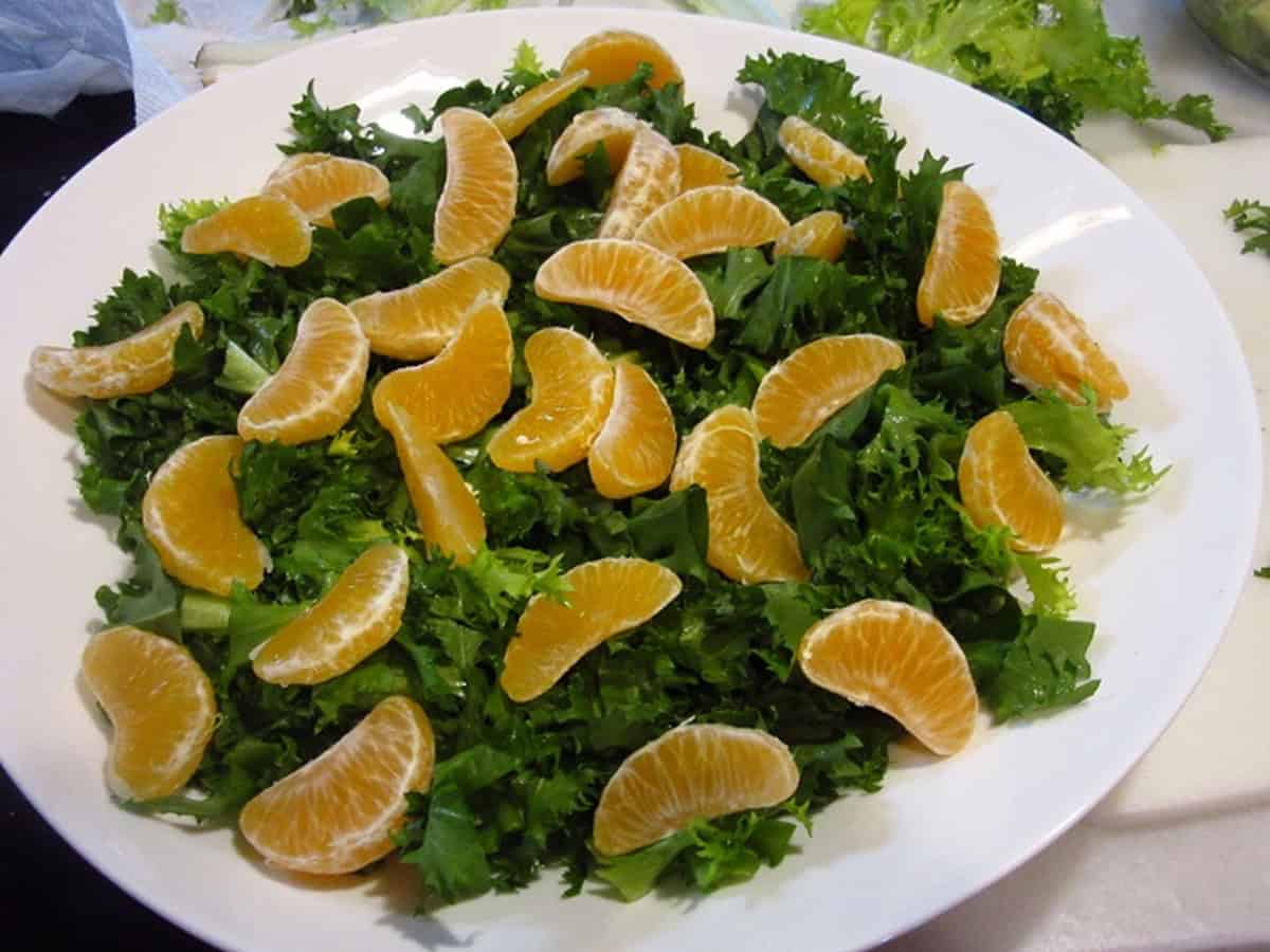 Mandarin orange segments and dark green endive lettuce in a white bowl.