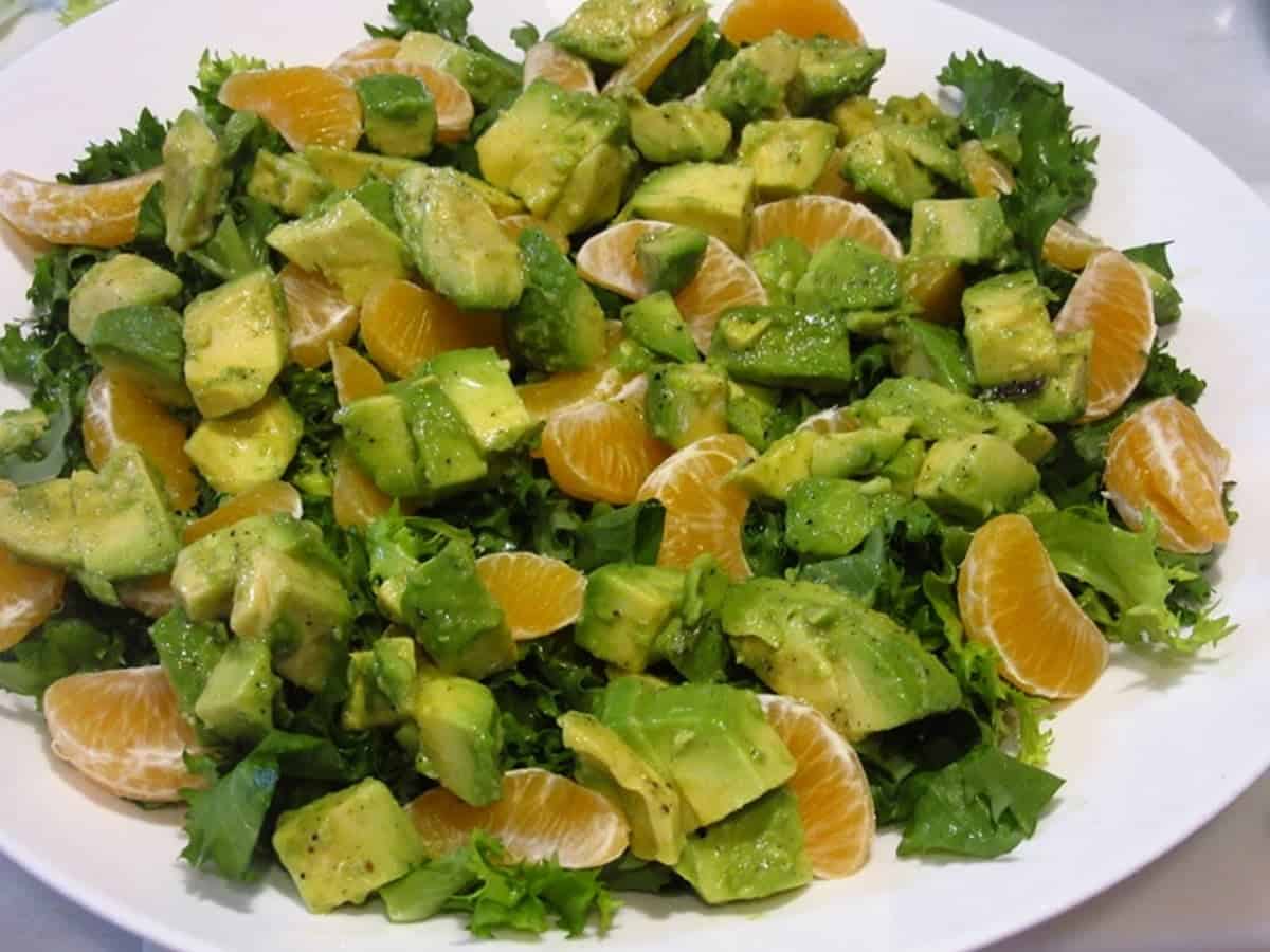A salad with diced avocado, mandarin orange segments and lettuce in a white bowl.